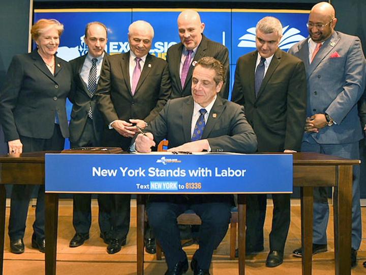 Gov. Andrew Cuomo signs a bill, flanked by union leaders, including UFT President Michael Mulgrew (directly behind Cuomo)