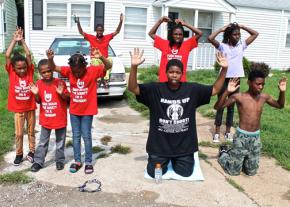 Black youth in Ferguson kneeling with hands up to protest the murder of Mike Brown