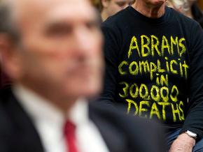 A protester sits behind Elliott Abrams during a House Foreign Affairs Subcommittee hearing